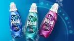 A blue, turqouise and pink bottle of Persil Wonder Wash on a teal backdrop.