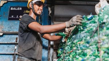 A worker in a hard hat and gloves smiles while arranging plastics