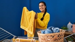 A women in yellow jumper doing laundry holding a yellow towel.