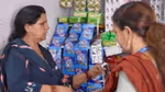 Two women talking at a shop counter with various products displayed.