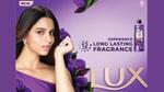 A woman in a purple dress posing with purple flowers, next to a Lux body wash bottle.