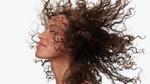 Side profile headshot of woman throwing her head back to showcase the condition of her long, mid-brown naturally curly hair